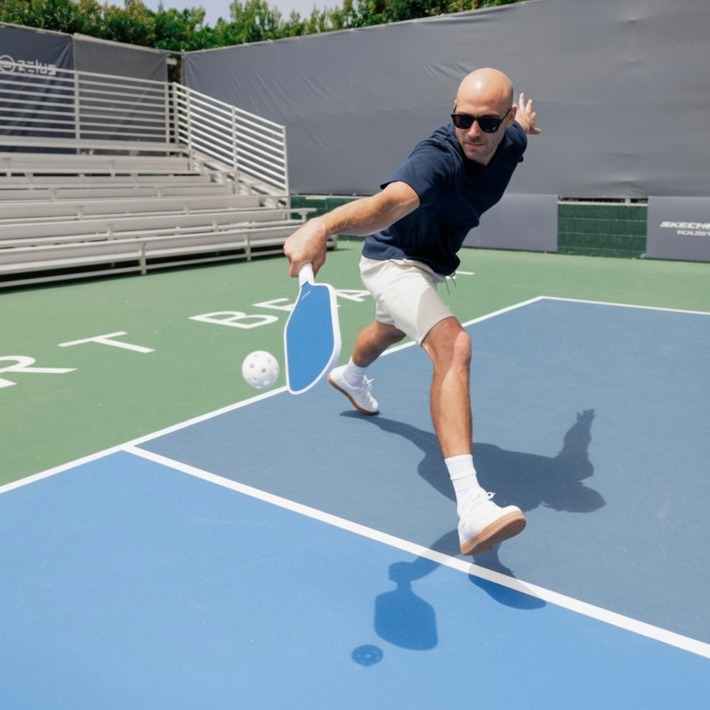 Man playing pickleball on an outdoor court with a blue paddle and white ball.